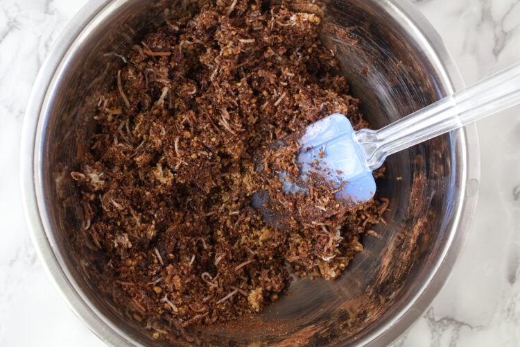 a bowl with a spatula, cocoa powder, graham cracker crumbs, coconut and melted butter mixed 